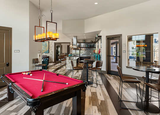 A pool table is in the middle of a room with a bar and chairs.