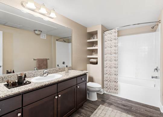 A bathroom with a sink, mirror, toilet, and shower.