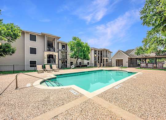 A swimming pool surrounded by a gravel area and apartment buildings.