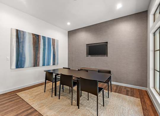 A modern meeting room with a large painting on the wall and a flat screen TV above the table.