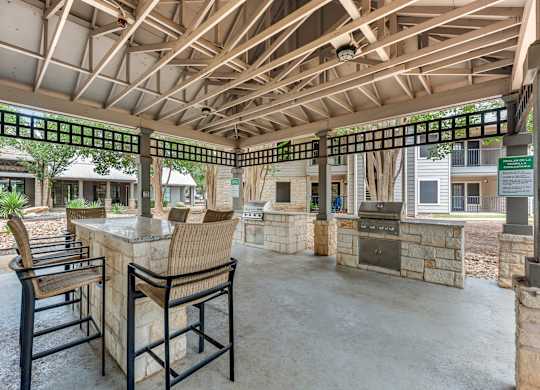A patio with a table and chairs under a wooden roof.