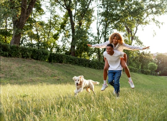 a man and woman running through a field with a dog