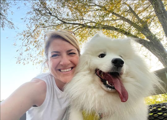 a woman holding a white dog with its tongue out
