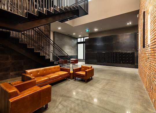 A brown leather couch sits in a room with a black staircase.at Raymond Block, Edmonton, AB T6E 3R7