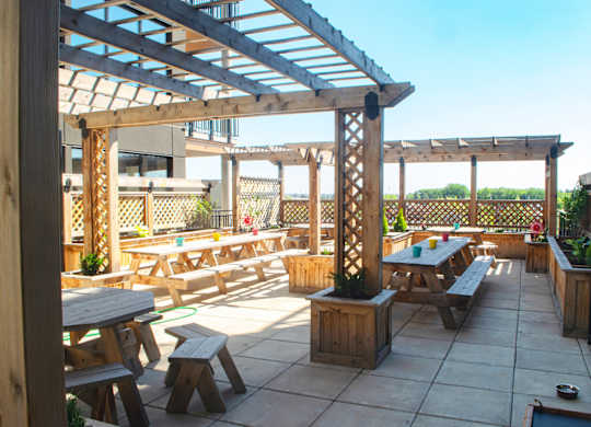 A wooden pergola with benches and picnic tables is set up on a patio.at Raymond Block, Alberta, T6E 3R7
