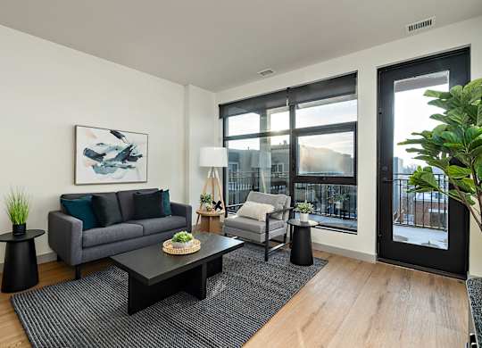 A modern living room with a grey couch, a coffee table, and a large window.at Raymond Block, Edmonton, AB