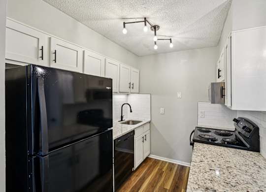 A black fridge and stove in a small kitchen.