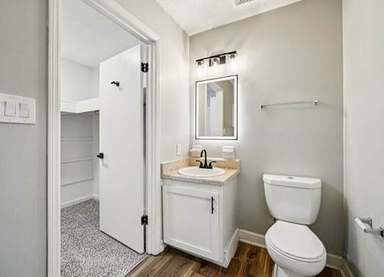 A white bathroom with a toilet, sink, mirror, and a door.