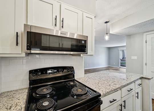 A black stove top oven with four burners is in a kitchen with white cabinets.