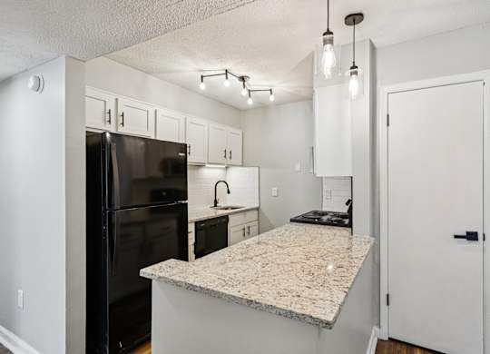 A kitchen with a granite countertop and a black refrigerator.