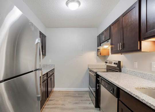 A kitchen with a stainless steel refrigerator and dark brown cabinets at The Onyx Hoover Apartments, Hoover, AL