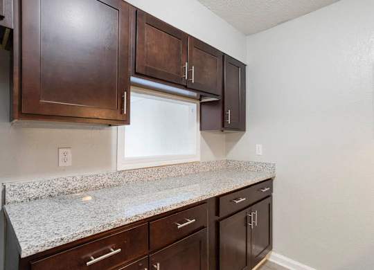 A kitchen with brown cabinets and granite countertops at The Onyx Hoover Apartments, Hoover, AL