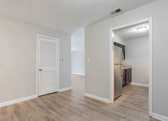 A room with a white door and a kitchen area in the background. at The Onyx Hoover Apartments, Hoover, AL