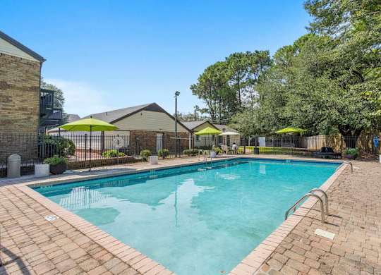 A large outdoor swimming pool surrounded by a brick patio and trees at The Onyx Hoover Apartments, Hoover, 35216