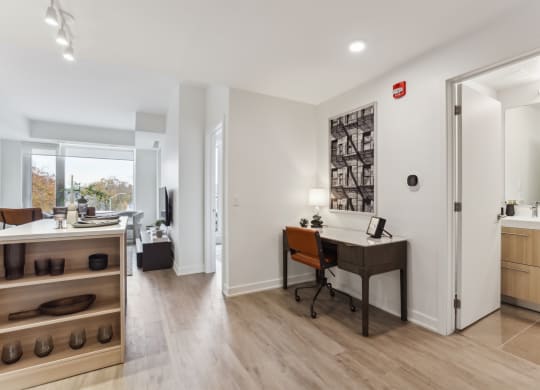 a home office with a desk and a doorway to a living room
