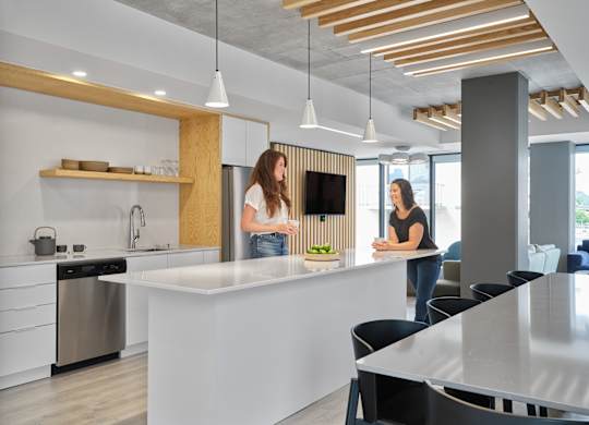 Two women are standing in a modern kitchen with a white countertop and wooden accents.