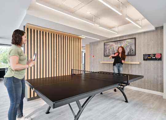 A woman is playing ping pong in a room with a wooden wall.