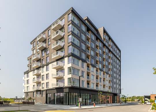 A modern multi-story residential building with balconies and a black entrance.