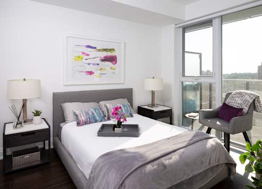 A bedroom with a large bed, two lamps, a painting, and a chair.