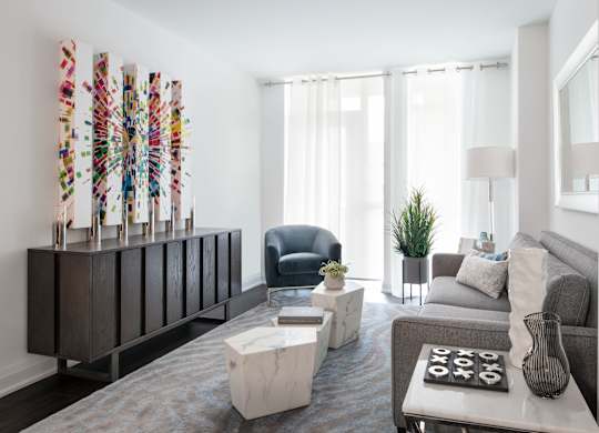 A living room with a grey couch, a white coffee table, and a wooden cabinet with a colorful decoration on top.