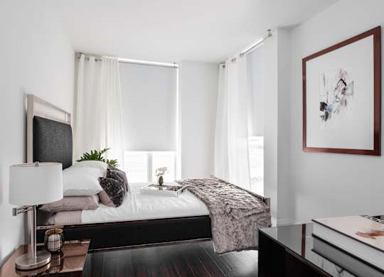 A modern bedroom with a large bed, a nightstand with a lamp, and a framed picture on the wall.