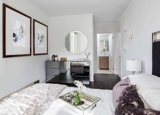 A bedroom with a large bed, a dresser, a mirror, and two framed pictures on the wall.