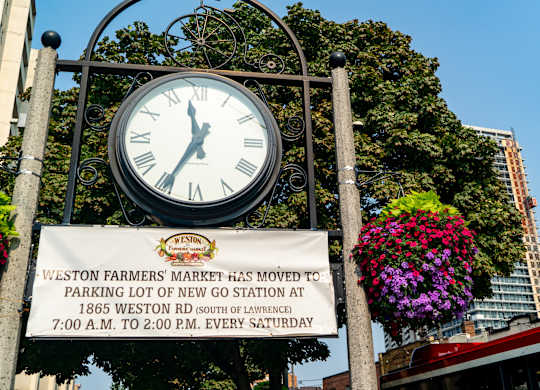 a large clock in front of a sign for the west end farmers market