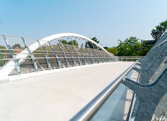 A pedestrian bridge with a metal railing and a white arched design.