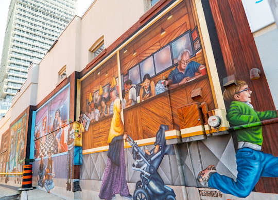 A mural on a building shows a man in a green shirt and blue jeans climbing a wall.