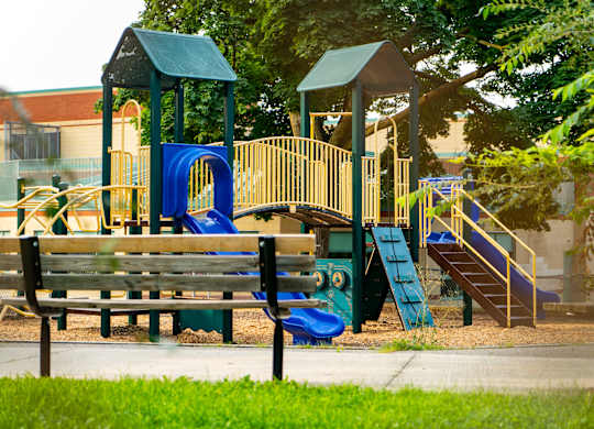 a playground with a bench and slides in front of a building