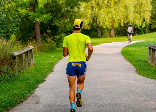 A man in a yellow shirt and blue shorts is running on a path in a park.