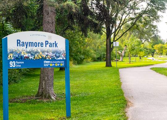 A sign for Raymore Park stands in a grassy area.