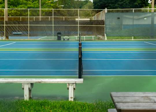 A tennis court with a bench and a trash can in the background.