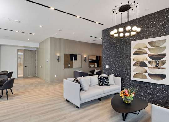 A modern living room with a grey sofa, a black coffee table, and a dining table with chairs.