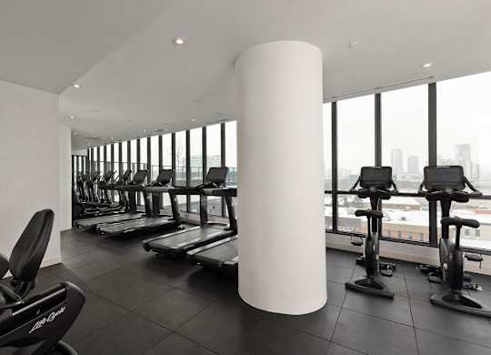 A gym with treadmills, exercise bikes and a large window.