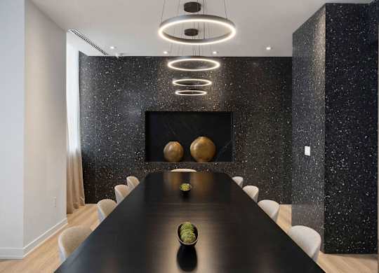 A long black table with a bowl of fruit on it and a black wall with a gold sphere and a black and white speckled design.