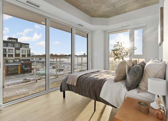 A bedroom with a large bed and a view of a cityscape through the windows.