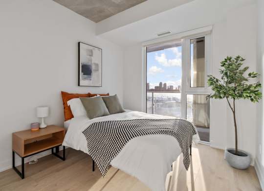 A bedroom with a bed, a nightstand, and a window overlooking a cityscape.