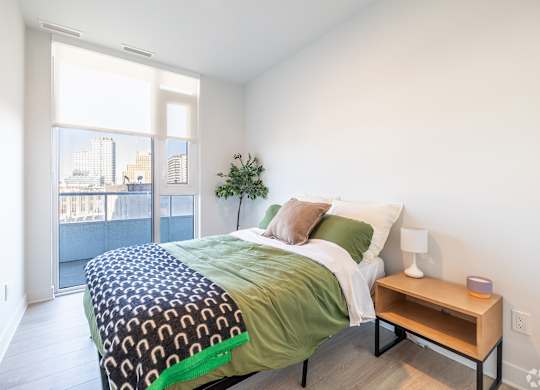 A bedroom with a bed, nightstand, and a plant.