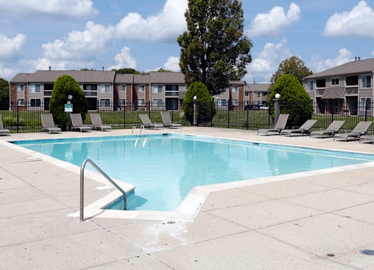 a swimming pool with chaise lounge chairs and apartment buildings in the background