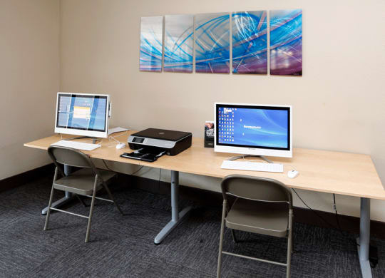two computers and a printer sit on a table in a room with two paintings on the wall