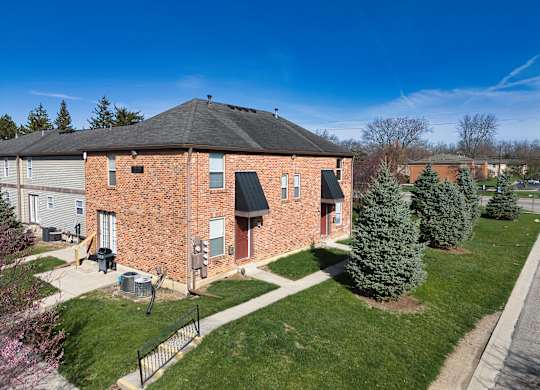a brick building with a black roof and a green lawn and trees