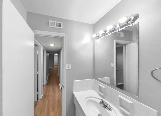 a bathroom with a sink and a mirror and a hallway