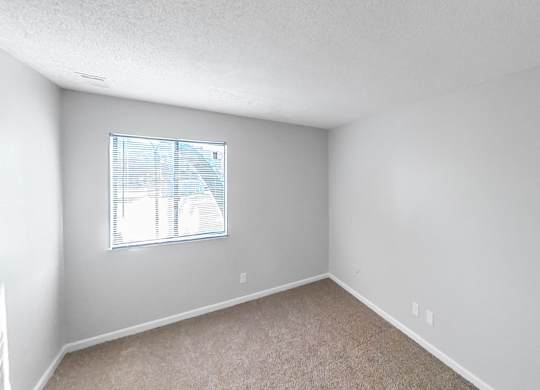 an empty bedroom with a window and carpeting