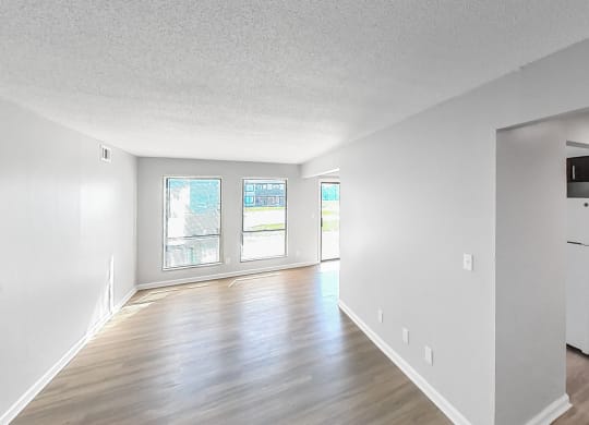 the living room and dining room of an apartment with white walls and wood floors