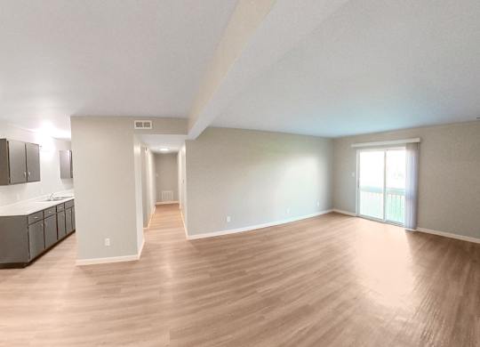 an empty living room with wood flooring and a kitchen