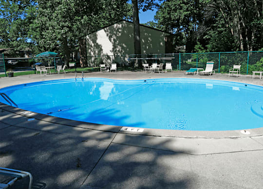 a large swimming pool with a fence around it and a patio with chairs and umbrellas