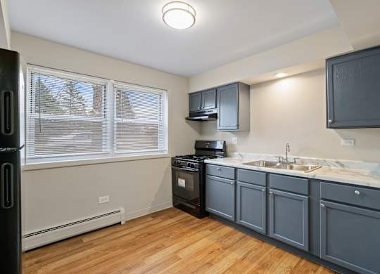 a kitchen with blue cabinets and a sink and a window at Hanover Park Blu Apartments, Illinois
