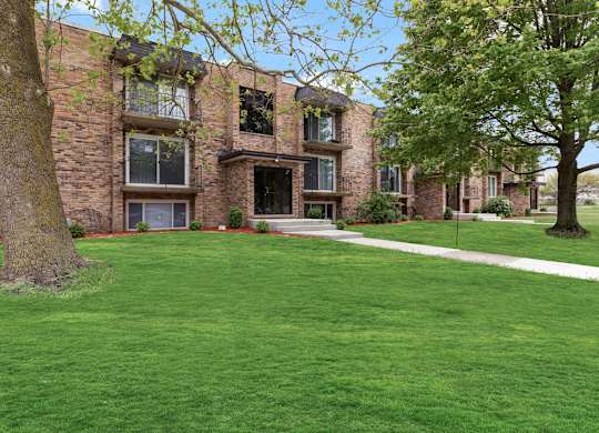 exterior view of a brick apartment building with green grass and trees