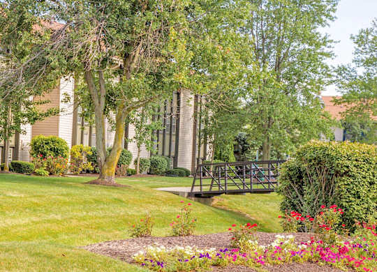 a bridge in front of a building with trees and flowers